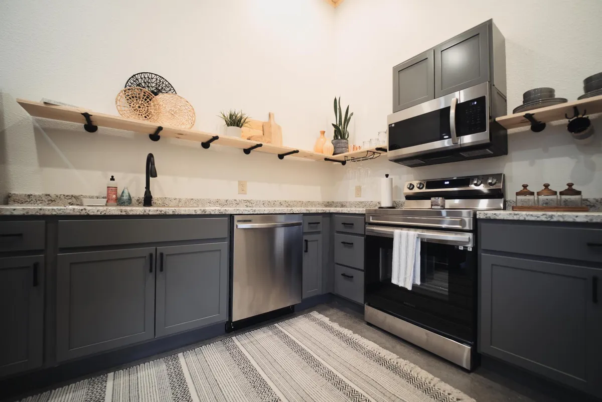 A bright and welcoming kitchen space with stainless steel appliances, a granite countertop, open shelving, and decorative plants. The scene suggests a hub for family gatherings, preparing snacks for day trips, or sharing meals after exploring the area.
