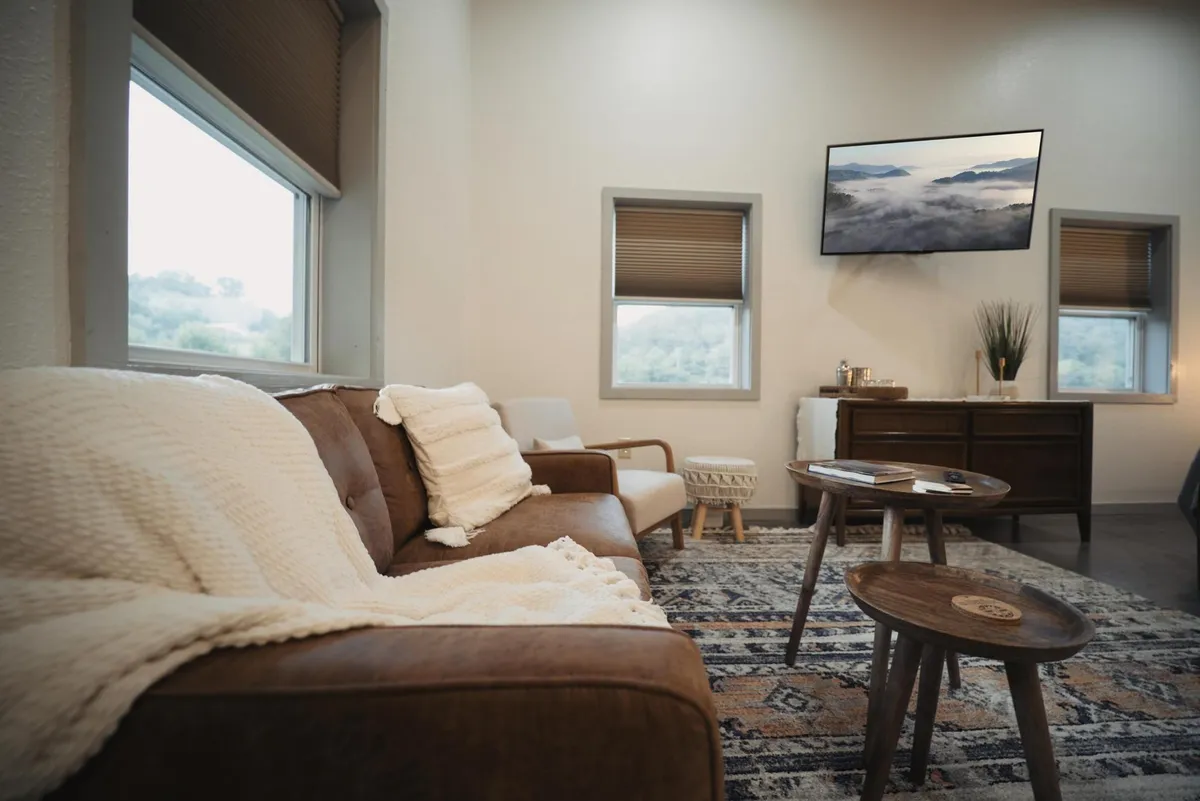 A stylish living area centered around a leather sofa with a decorative throw, two coffee tables, a wall-mounted television, and a soft rug. The design radiates warmth and comfort, perfect for movie nights or unwinding after a day of adventure.